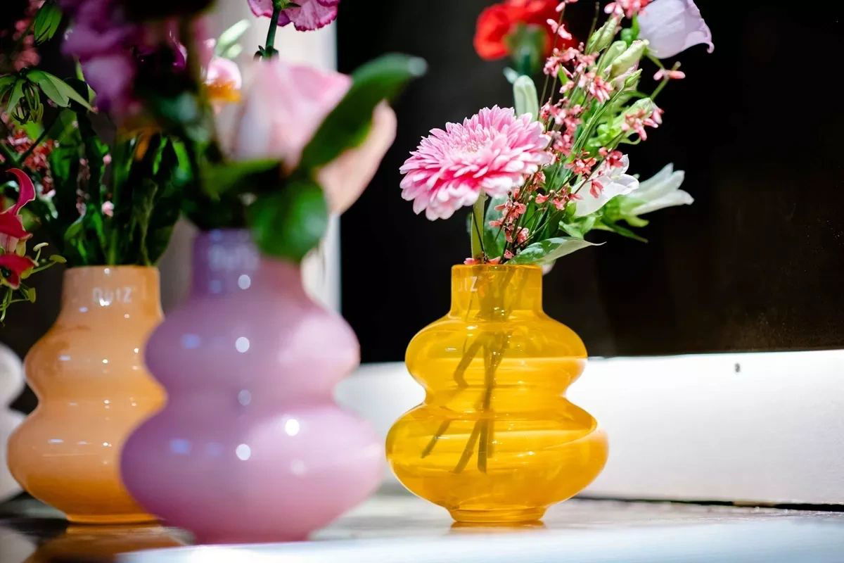 Lowlands Design yellow glass vase with pink and white flowers on a white surface