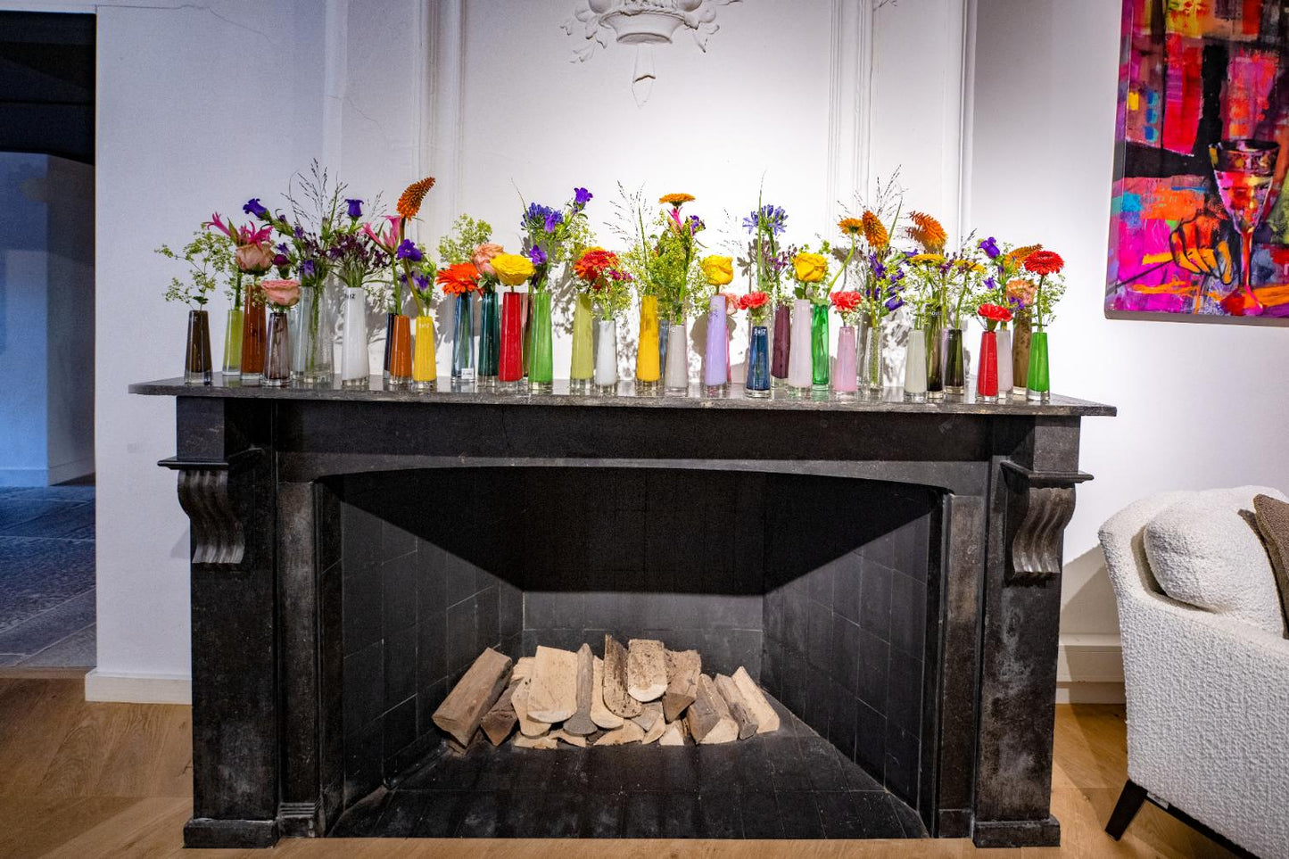 Display of vibrant single flower vase glass on a mantelpiece with various coloured vases