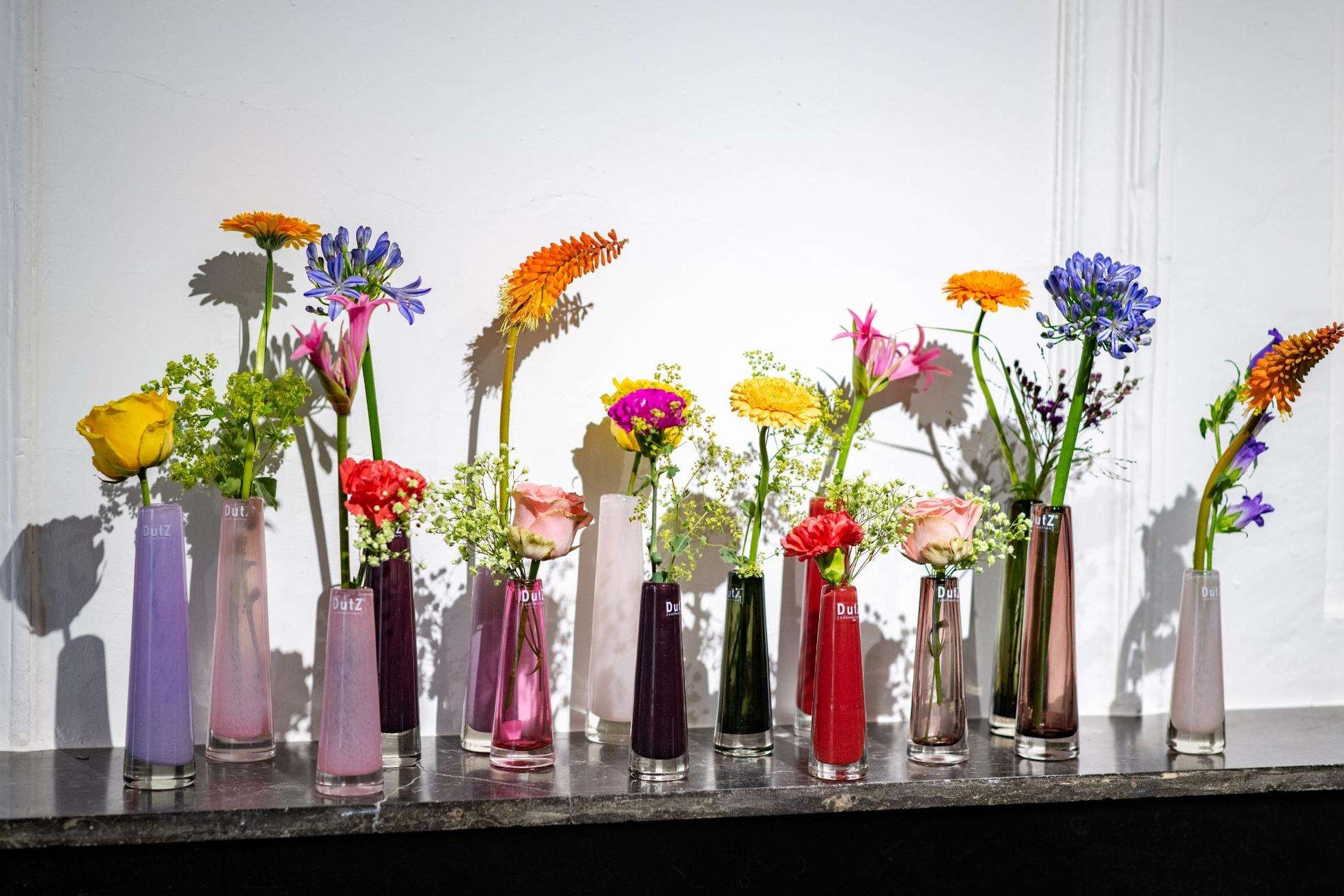 Collection of colourful solifleur vases in glass with various flowers, perfect for modern decor