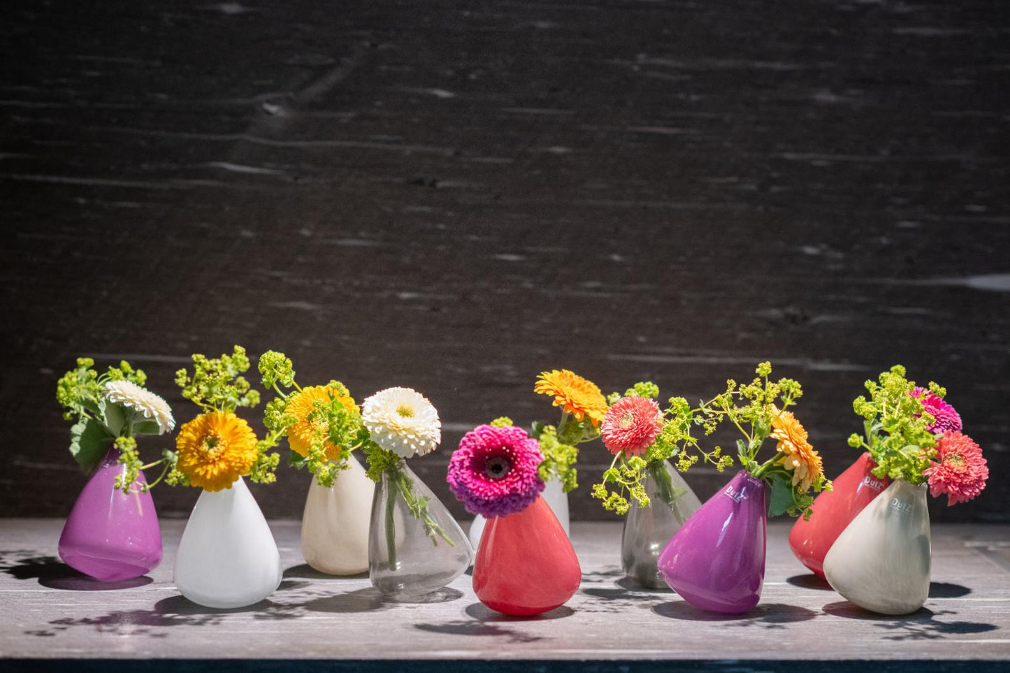 Set of tumbling vase glass in various colours with vibrant flowers, each 10cm tall
