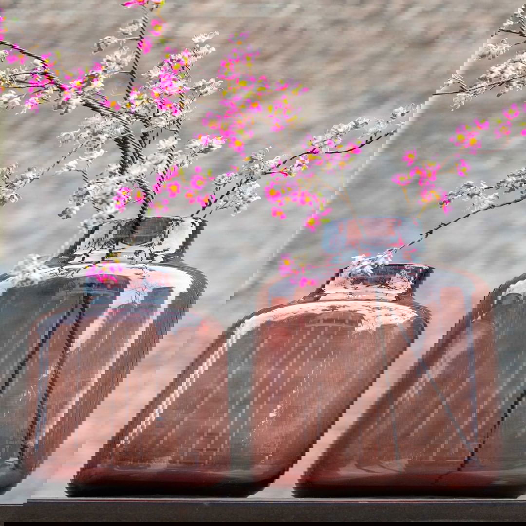 Two brown glass vases by Lowlands Design with pink cherry blossom branches on a wooden surface