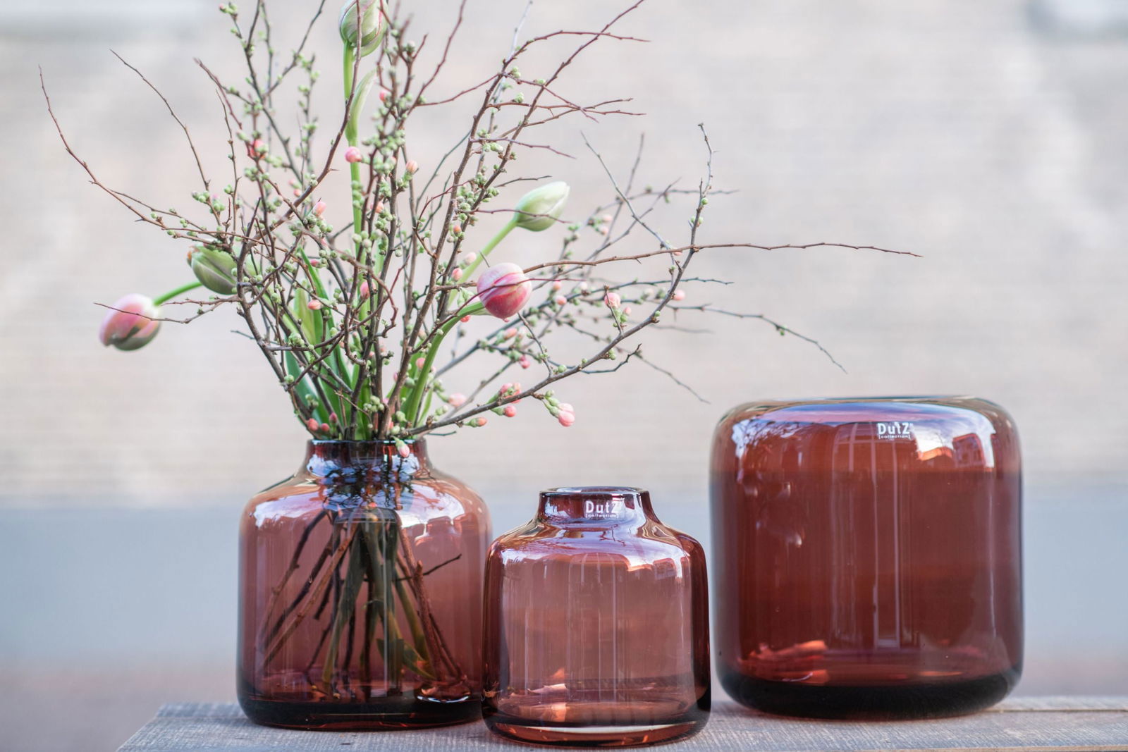 Set of three amber glass vases by Lowlands Design with one vase holding branches and flowers