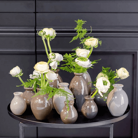 Lowlands Design ceramic vase set with neutral tones holding white flowers and green foliage on a black round table
