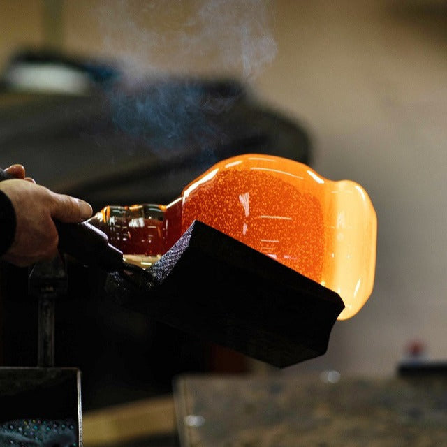 Glassblower shaping molten glass with smoke in the background