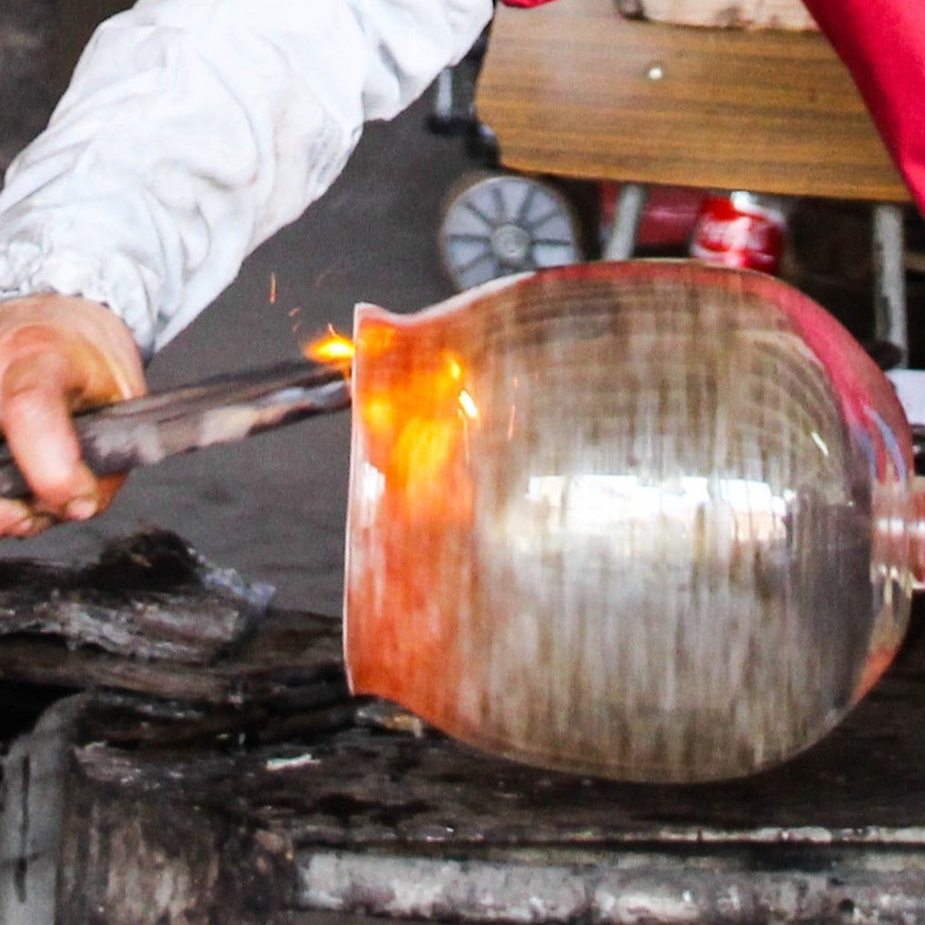 Glassblowing process with a glass object being worked on over a flame.