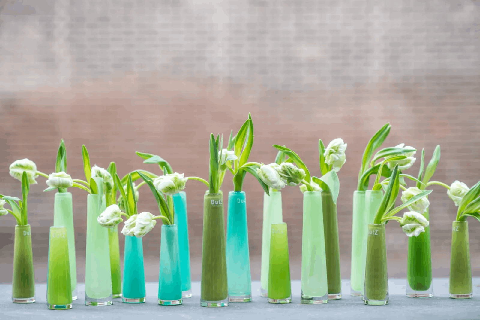 Collection of colourful Solifleur budvase by Lowlands Design holding white flowers on a grey surface