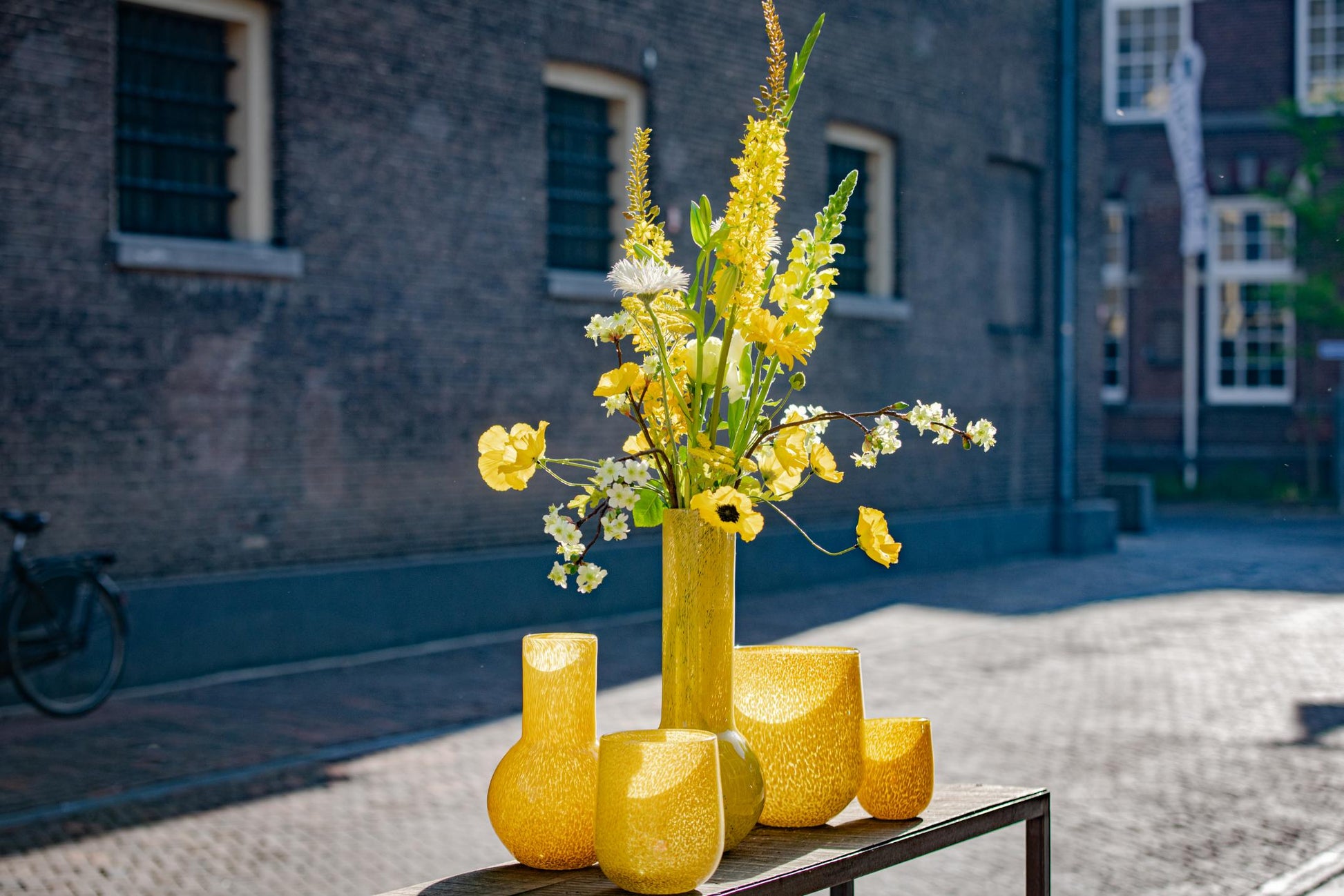 Yellow glass BARREL vase candleholder with vibrant flowers on display outdoors