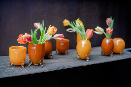 Lowlands Design vase set glass feet with orange and brown vases holding fresh tulips on a wooden surface